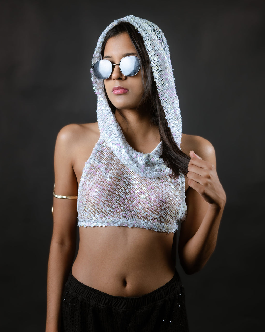 Woman wearing a sparkling silver hooded top and black pants against a dark background
