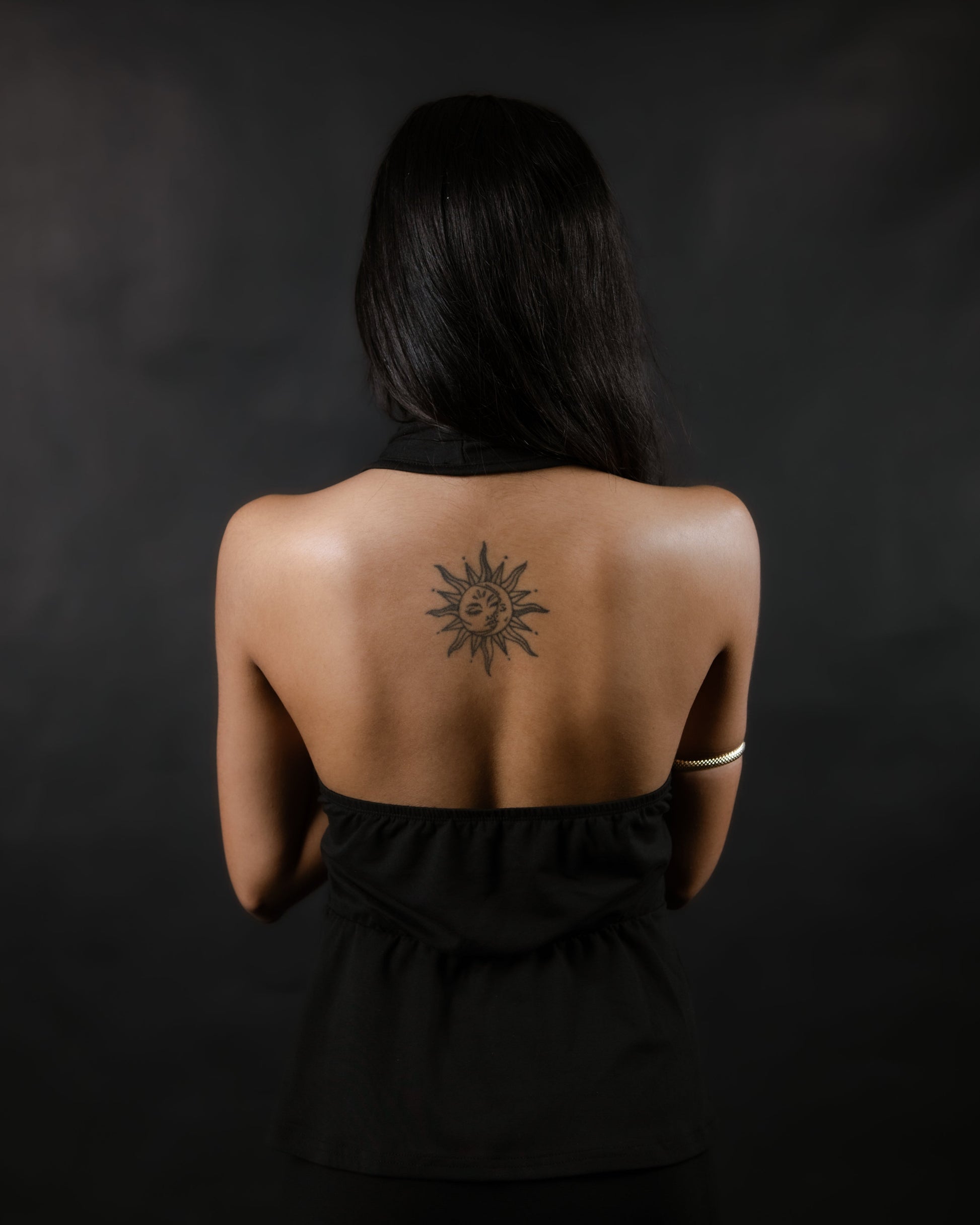 Woman with a sun tattoo on her back against a black background